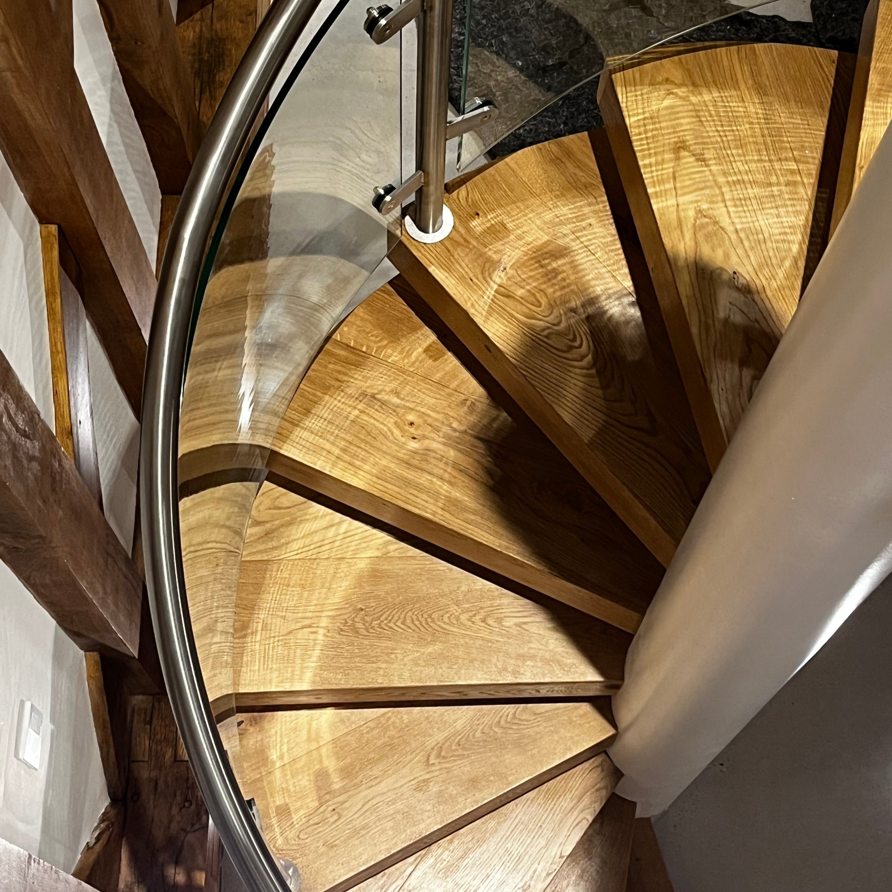 Metal feature staircase with radius glass balustrade in a modern interior setting. Wrap around engineered oak treads giving a clean and minimalistic feel
